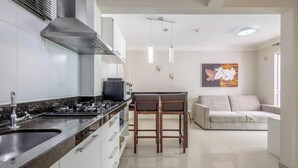 A modern kitchen with a gas stove, a microwave, and a built-in oven. There is a dining area with a table and two chairs. A sofa is placed in the living room area. - Beautiful Apt in a Cond. With Heated Pools Sbh0233 (Bombinhas)