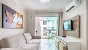 A modern living room with a sofa, a flat-screen TV mounted on the wall, and a dining area with chairs. - Beautiful Apt in a Cond. With Heated Pools Sbh0233 (Bombinhas)