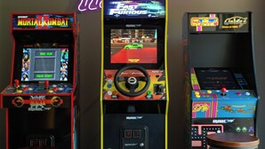 Tres máquinas de videojuegos con letreros de neón, un joystick y una pantalla mostrando un juego de carreras.