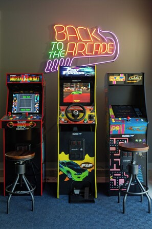 Three arcade machines with neon signs, a joystick, and a screen displaying a racing game. - The Dutch at Black Barn Ridge : Luxury Wellness in the Woods (Saugatuck)