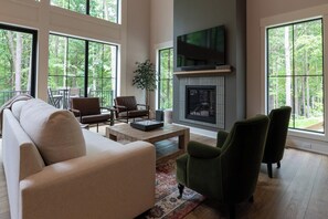 A spacious living room with a fireplace, large windows, and a television. - The Dutch at Black Barn Ridge : Luxury Wellness in the Woods (Saugatuck)