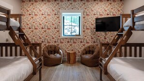 Una habitación con literas, dos sillones de mimbre, una pequeña mesa de madera y un televisor montado en la pared.