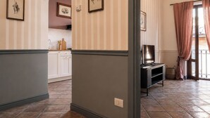 A hallway with striped wallpaper, a dining area with white cabinets, and a television on a stand. - Old Town Elegant Apartment in Anguillara (Anguillara Sabazia)