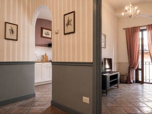 Ein Flur mit gestreifter Tapete, ein Essbereich mit weißen Schränken und ein Fernseher auf einem Schrank.