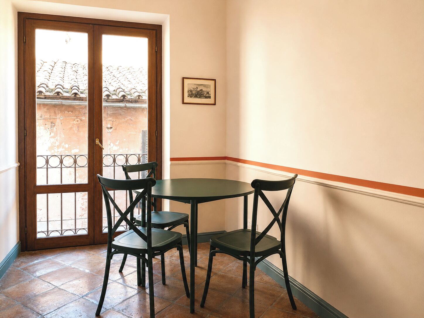 A room with a table and four chairs, a door with a view to an outdoor area, and a framed picture on the wall.