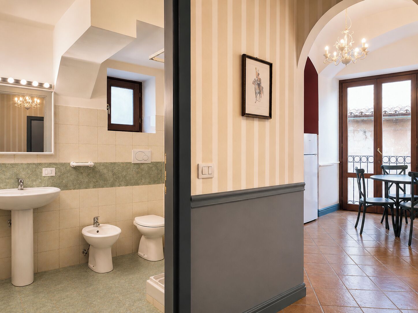 Un baño con lavamanos, bidé e inodoro, un espejo con luces y un cuadro en la pared.