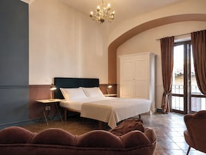 A hotel room with a bed, a wardrobe, a chandelier, and a view through a window.