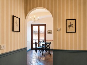 Ein Korridor mit gestreifter Tapete, einer Chandelüster, gerahmten Bildern und Blick durch eine Tür.