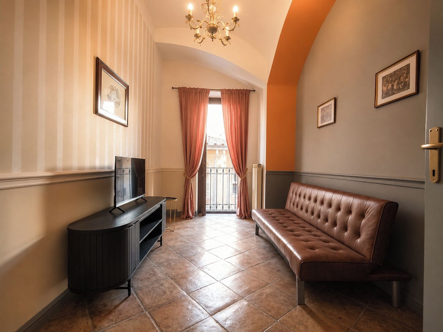 Un'hall dell'hotel con televisore, un divano in pelle marrone, un lampadario e una vista attraverso una finestra con tende.