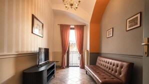 A hotel lobby with a television, a brown leather sofa, a chandelier, and a view through a window with curtains. - Old Town Elegant Apartment in Anguillara (Anguillara Sabazia)