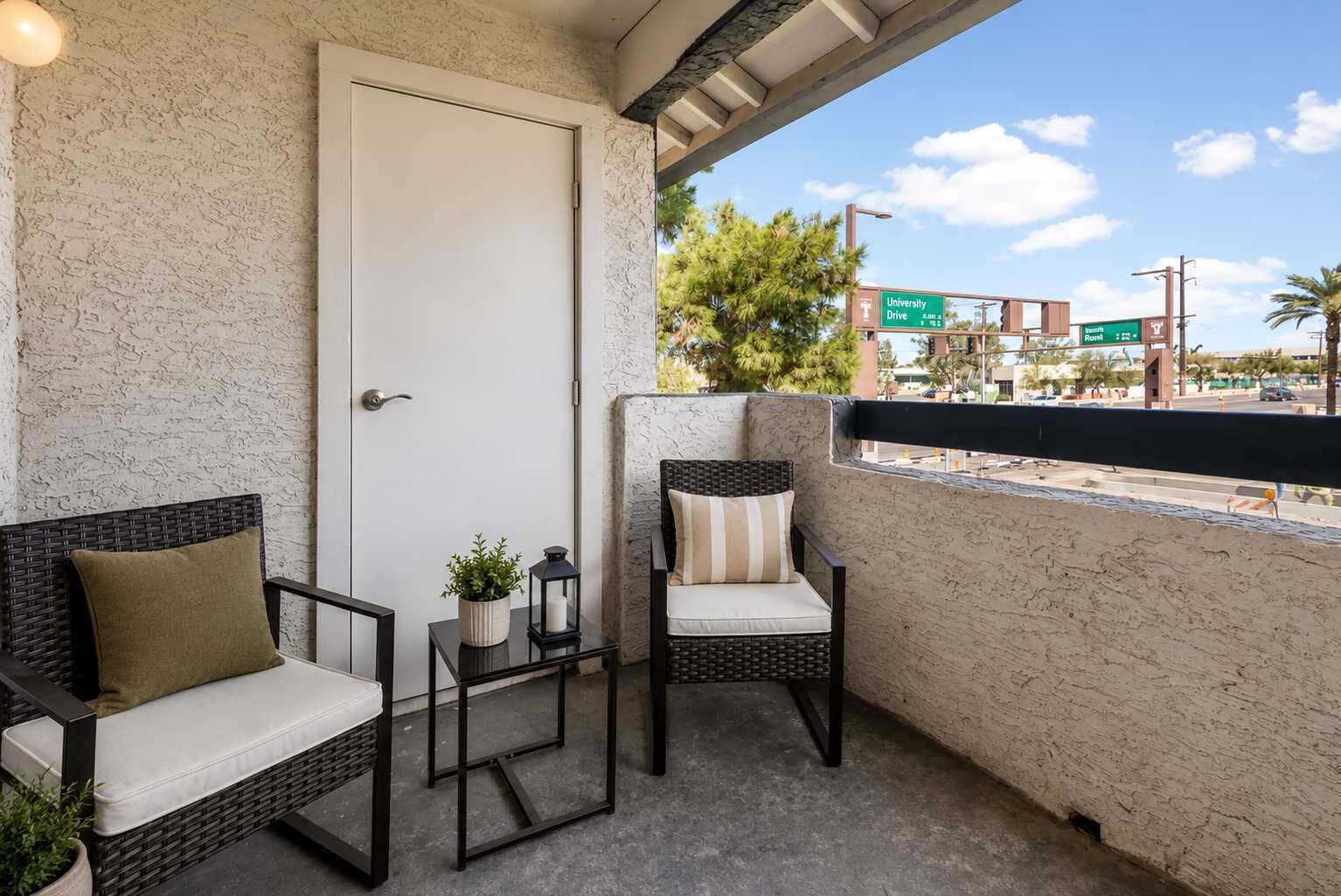 Un balcón con mobiliario de mimbre, una puerta y vista a una calle con un letrero que dice 'University Drive'.