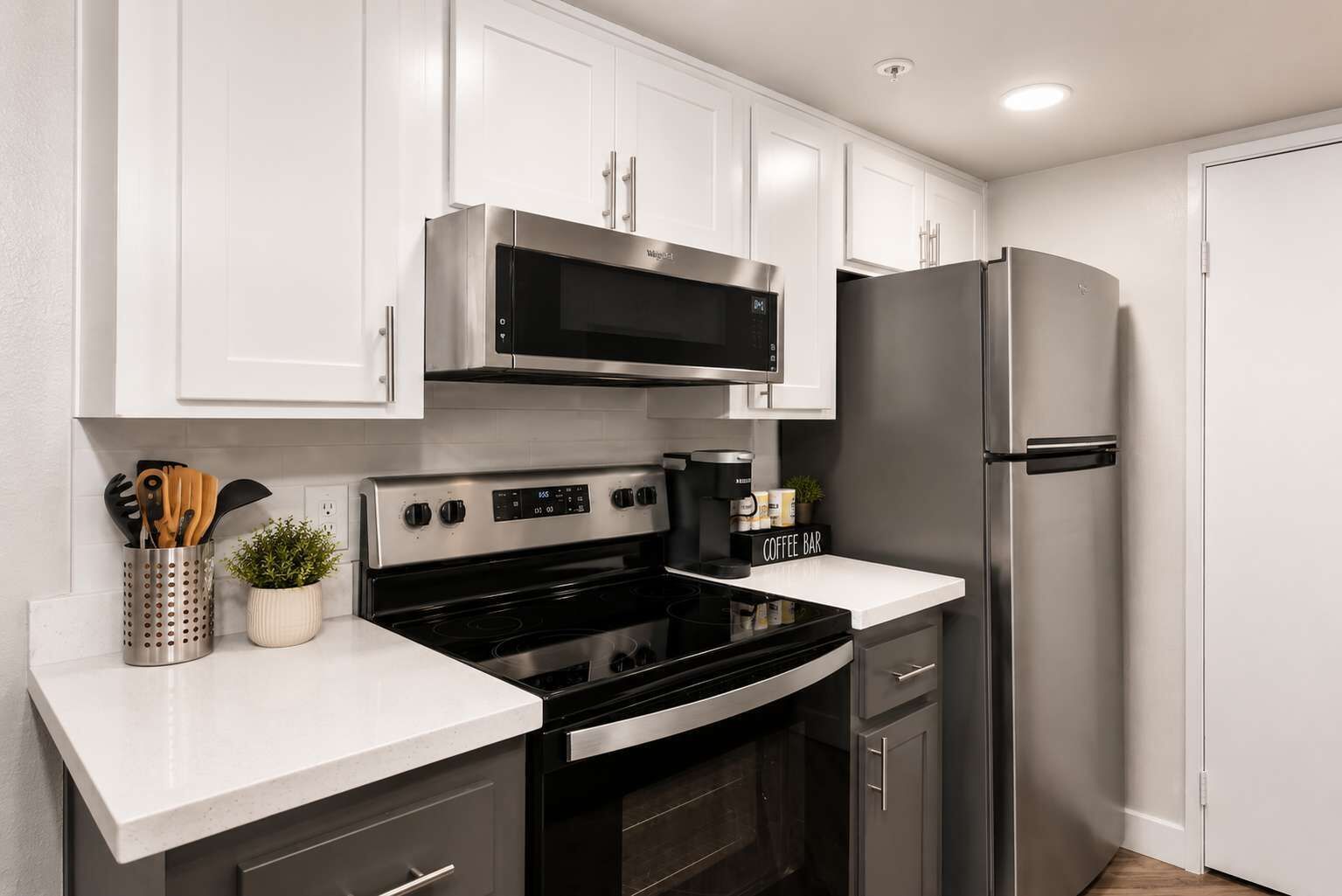 A modern kitchen with white cabinets, a stainless steel refrigerator, a microwave, and a stove.