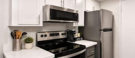 A modern kitchen with white cabinets, a stainless steel refrigerator, a microwave, and a stove.