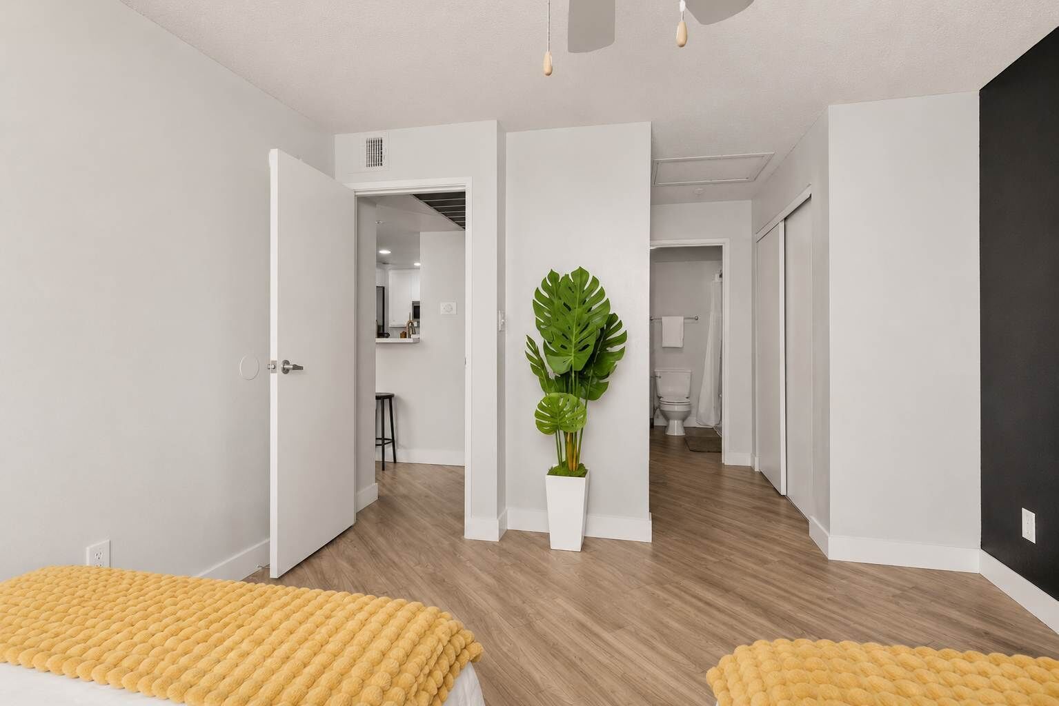 Une chambre d’hôtel moderne avec un plancher en bois, une grande plante en pot et un plaid jaune.