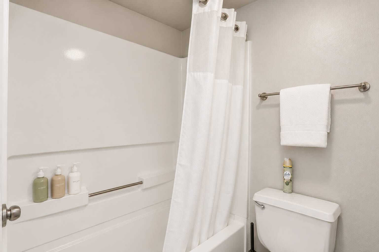 Un baño con cortina de ducha, inodoro, toallero y estante con artículos de aseo.
