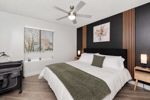 A hotel room with a bed, a ceiling fan, a window with blinds, a bedside table with a lamp, and a wall-mounted artwork. - Modern Tempe Retreat Near ASU Pool, Gym, Pet-Friendly, Parking (Tempe)