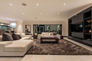A modern living room with a beige sofa, a coffee table, and a large flat-screen TV mounted on the wall. - Luxury Coastal Retreat (Knysna)
