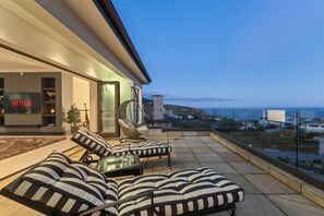 A modern outdoor seating area with striped cushions and a glass table, overlooking a scenic view of a coastal landscape. - Luxury Coastal Retreat (Knysna)