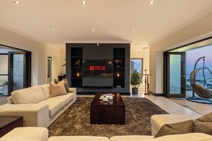 A modern living room with a flat-screen TV, a sofa, a coffee table, and a large window with a view. - Luxury Coastal Retreat (Knysna)