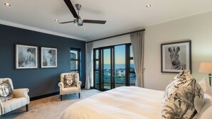 Quarto com uma cama grande, uma cadeira, um ventilador de teto e obras de arte nas paredes.