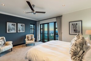A bedroom with a large bed, a chair, a ceiling fan, and artwork on the walls. - Luxury Coastal Retreat (Knysna)