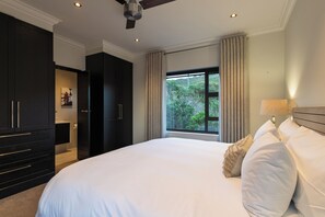 A bedroom with a large bed, a wardrobe, a bathroom, and a window with a view of greenery.