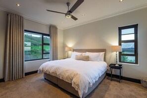 Ein Schlafzimmer mit einem Bett, zwei Nachttischlampen, einem Deckenventilator und Blick ins Grüne.