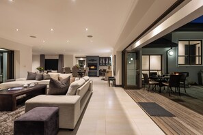 A modern living room with a fireplace, a dining area, and a view of the outdoors. - Luxury Coastal Retreat (Knysna)