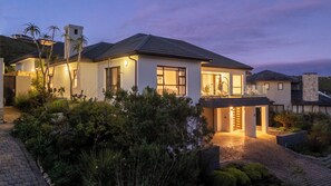 A modern two-story house with a well-lit entrance, a covered patio, and a landscaped garden.