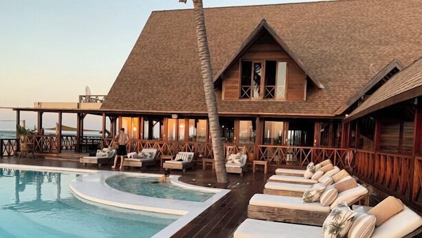 A poolside area with lounge chairs and a wooden building with a thatched roof. - Normal Property Name (Prague)