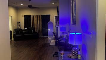 Un salon doté d’un parquet en bois foncé, d’un canapé en cuir noir, d’une table à manger avec une lampe et d’un ventilateur de plafond.