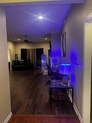 Un salon doté d’un parquet en bois foncé, d’un canapé en cuir noir, d’une table à manger avec une lampe et d’un ventilateur de plafond.