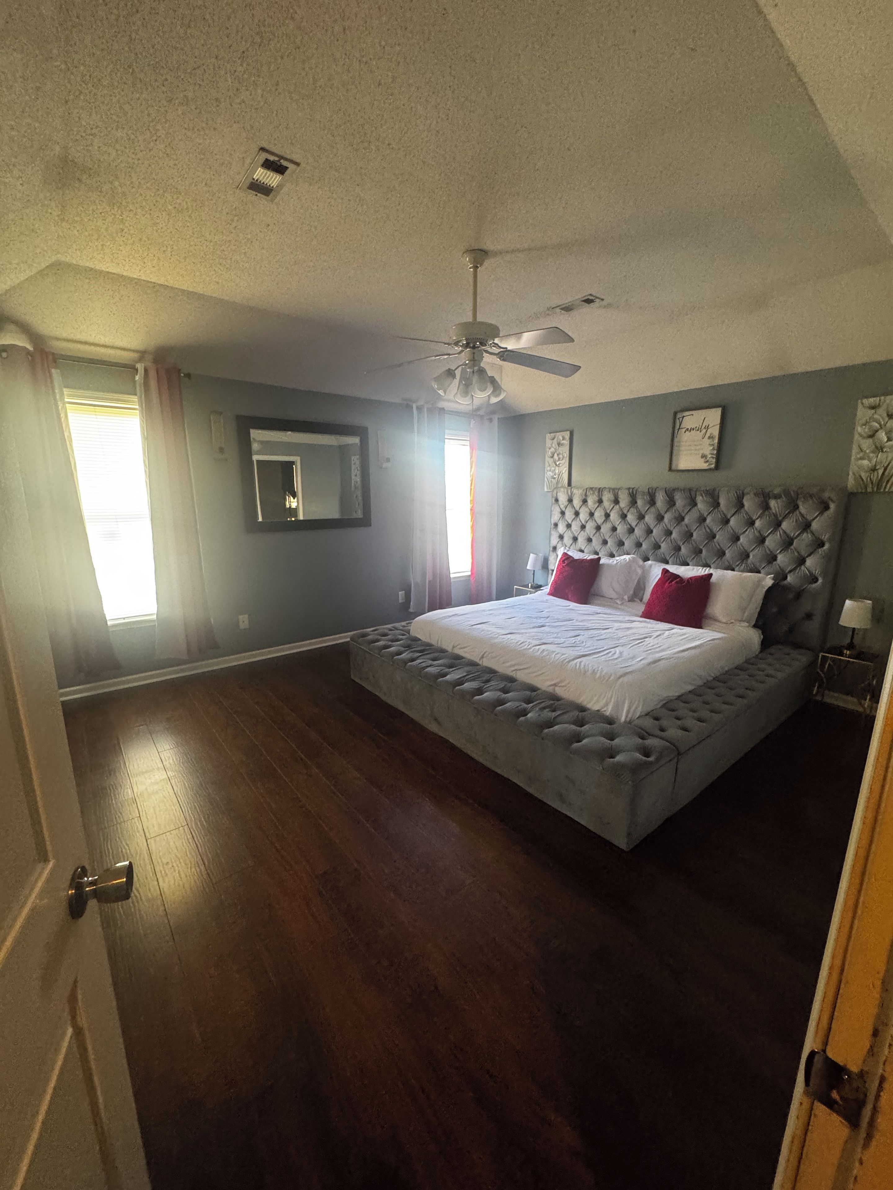 A bedroom with a large bed, a ceiling fan, and a window with curtains.