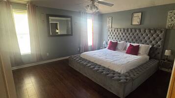 A bedroom with a large bed, a ceiling fan, and a window with curtains.