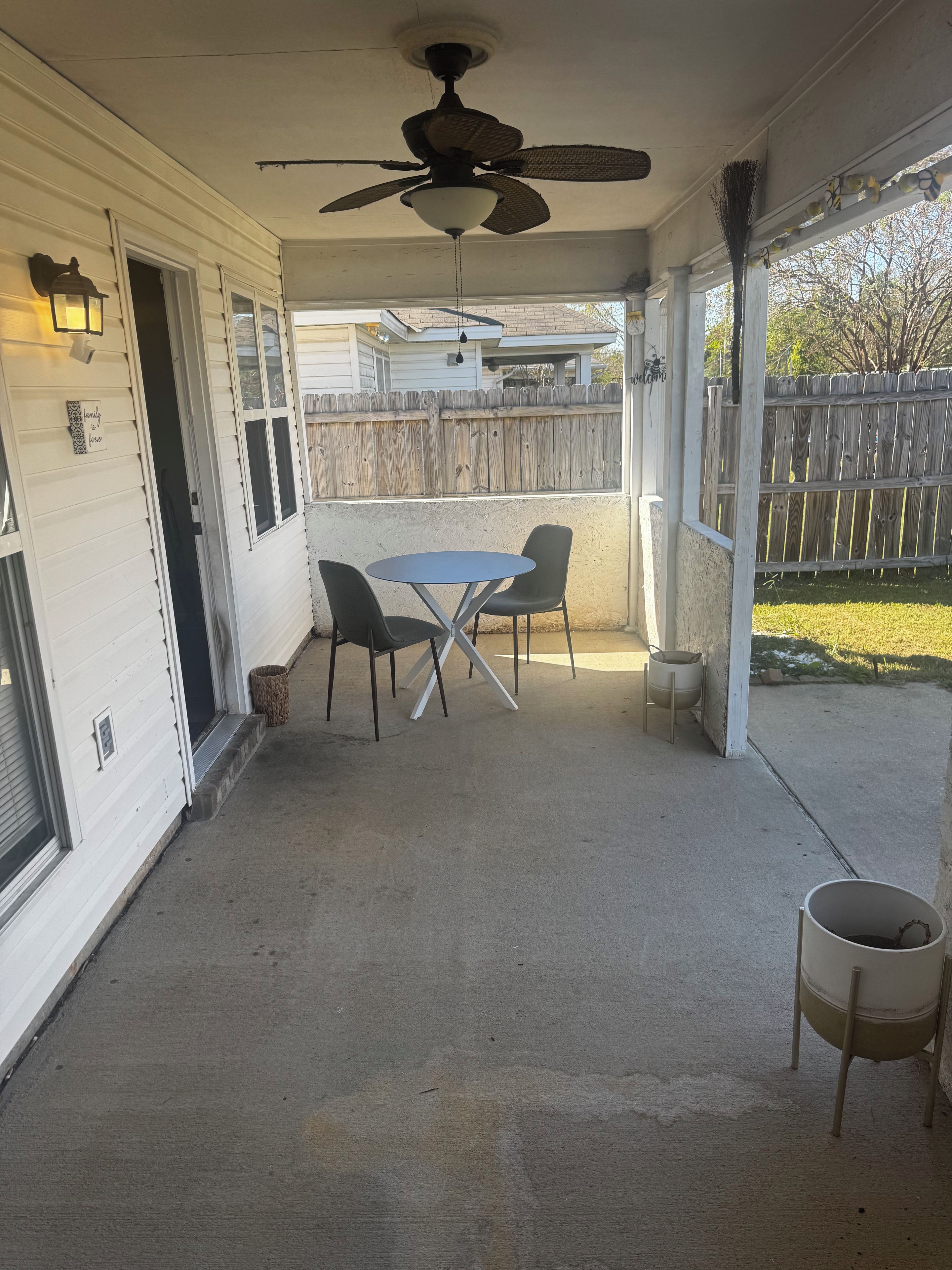 Eine überdachte Terrasse mit Deckenventilator, Tisch und Stühlen sowie einem Holzzaun im Hintergrund.