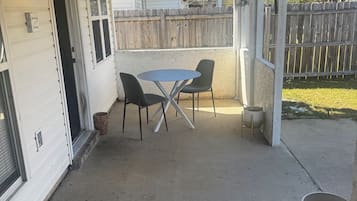 Eine überdachte Terrasse mit Deckenventilator, Tisch und Stühlen sowie einem Holzzaun im Hintergrund.