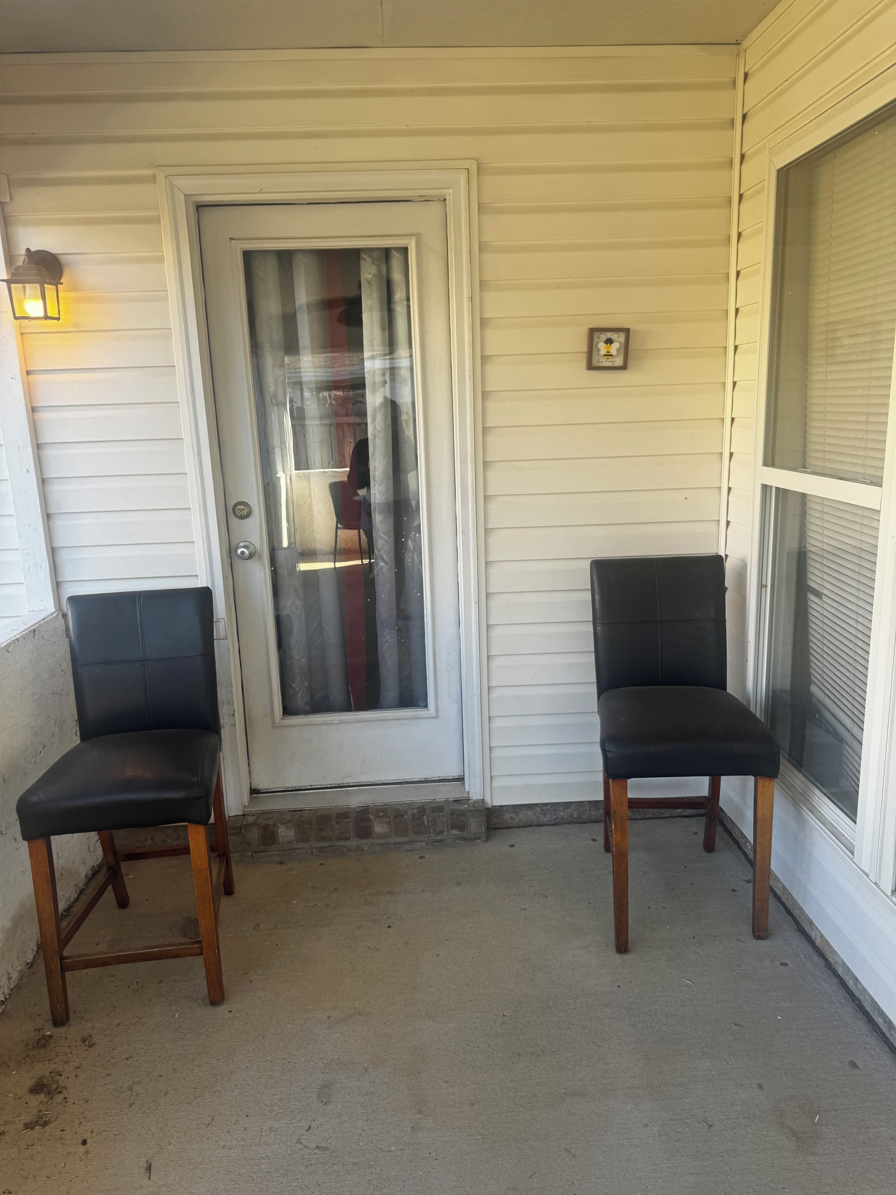 Eine Veranda mit zwei schwarzen Stühlen und einer weißen Tür mit Fensterglas.