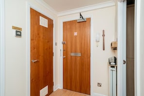 Un couloir avec deux portes en bois, un téléphone et une petite étagère sur laquelle sont posés divers objets.