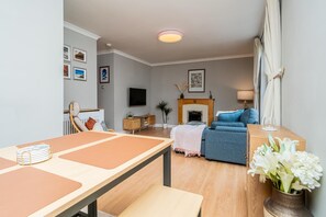 A living room with a sofa, a TV, a fireplace, and a dining area with a table and chairs. - Stylish Apartment | Minutes from the Royal Mile - Pass the Keys (Edinburgh)