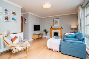 Un salon comprenant un canapé, un fauteuil, une cheminée, un téléviseur et des tableaux encadrés accrochés au mur.