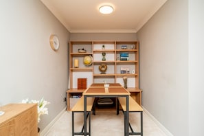 A small, well-lit room with a wooden desk, shelves with books and decorative items, a clock on the wall, and a vase with flowers on the desk. - Stylish Apartment | Minutes from the Royal Mile - Pass the Keys (Edinburgh)