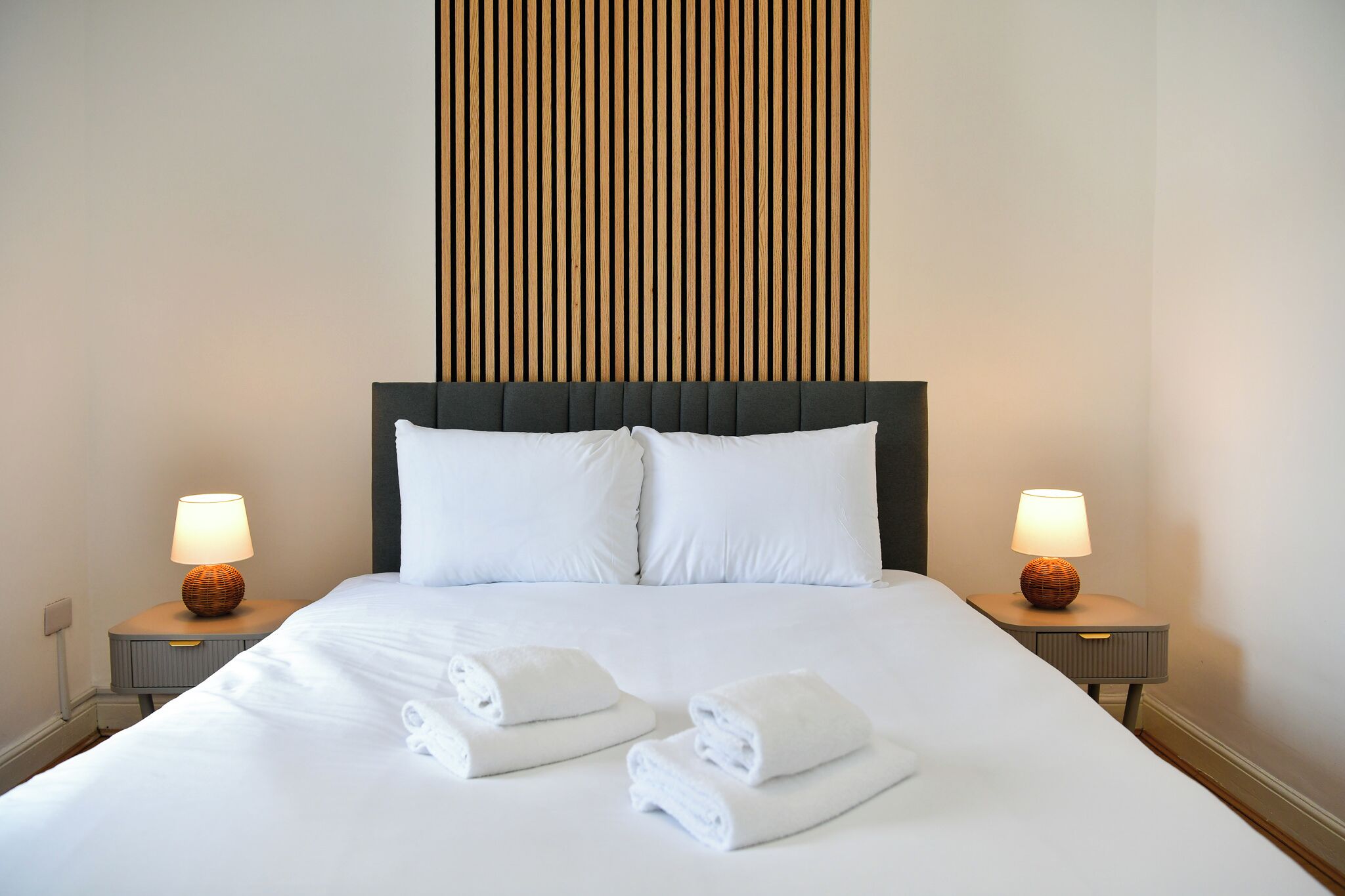 A neatly made bed with white linens and towels, flanked by two bedside lamps on matching nightstands.