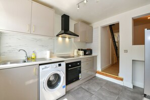 A modern kitchen with a built-in washing machine, a microwave, and a stove. - Spacious Modern 3-Bed House | Sleeps 6 - Pass the Keys (Cardiff)