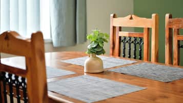 A wooden dining table with a vase of green plants, surrounded by four chairs with black metal backs.