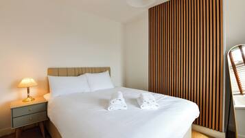 A hotel room with a bed, a nightstand with a lamp, and a wooden panel wall.
