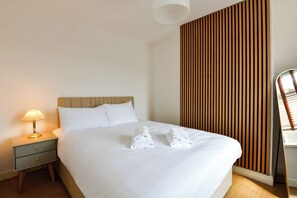 A hotel room with a bed, a nightstand with a lamp, and a wooden panel wall. - Spacious Modern 3-Bed House | Sleeps 6 - Pass the Keys (Cardiff)