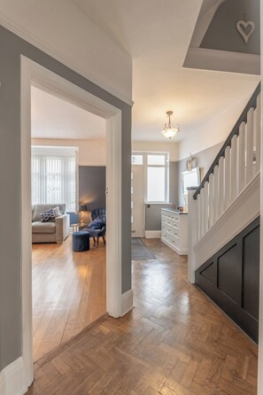 Uma sala de estar ampla com piso de madeira em padrão herringbone, uma poltrona azul escura e um sofá branco.