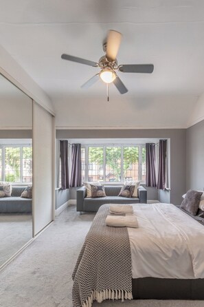 Quarto com cama, ventilador de teto, janela com cortinas e vista para o exterior.