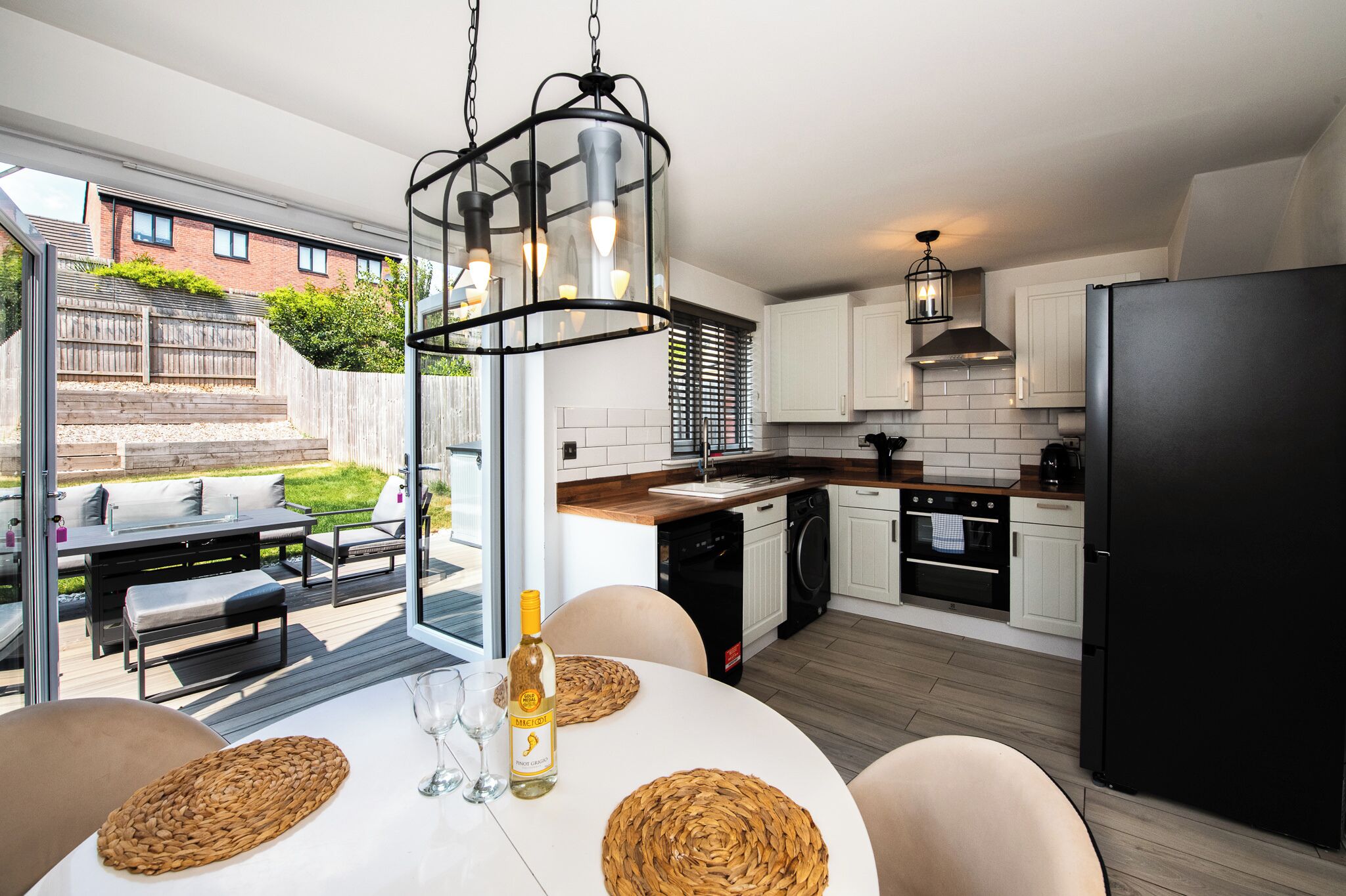 A modern kitchen with a dining area, featuring a large window, a built-in oven, and a black refrigerator.