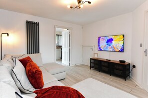 A modern living room with a sofa, a TV, and a dining area. - Stylish Family Home with Garden & Free Parking - Pass the Keys (Cardiff)